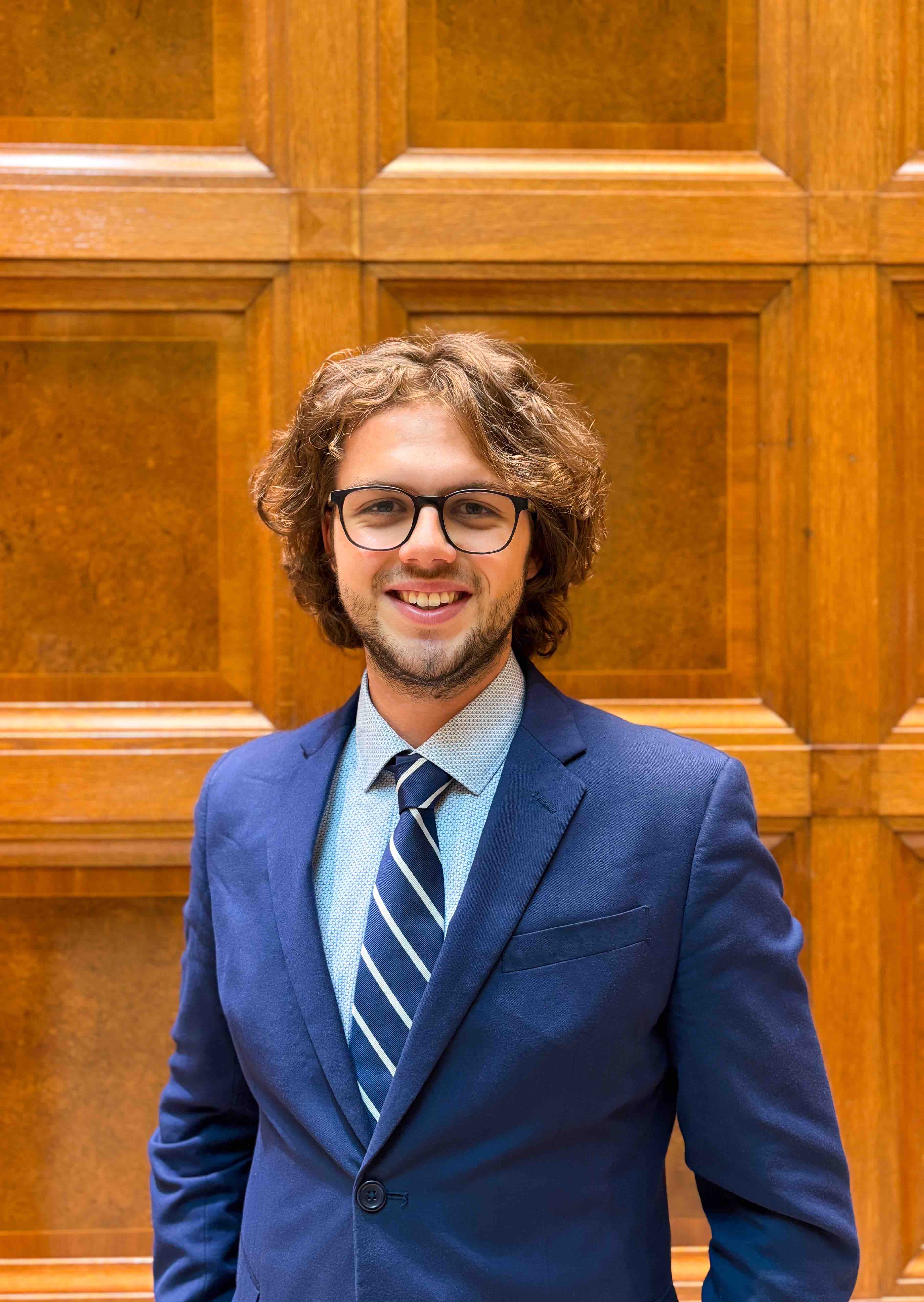 Vinzenz Antensteiner vor einer Holzwand mit Anzug